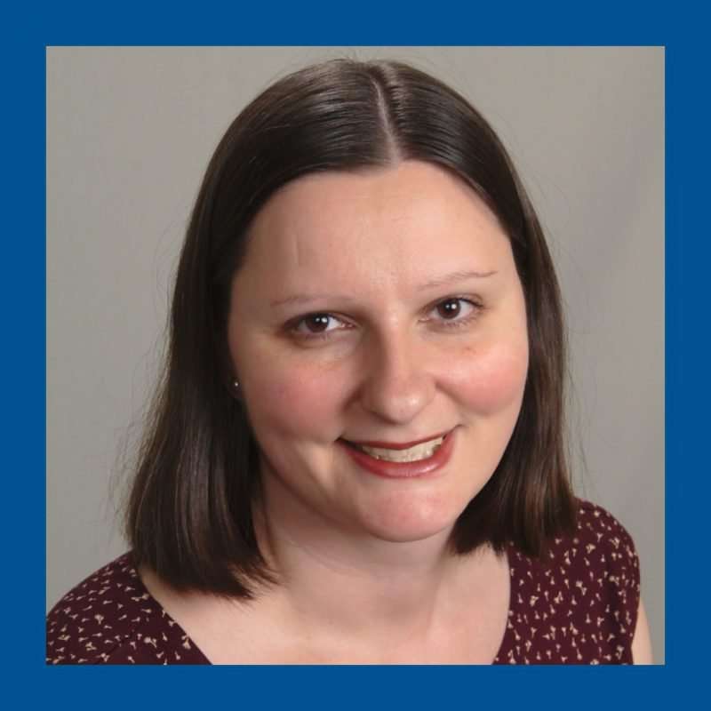 Grey background, blue frame. Woman with dark hair looking and smiling at the camera.