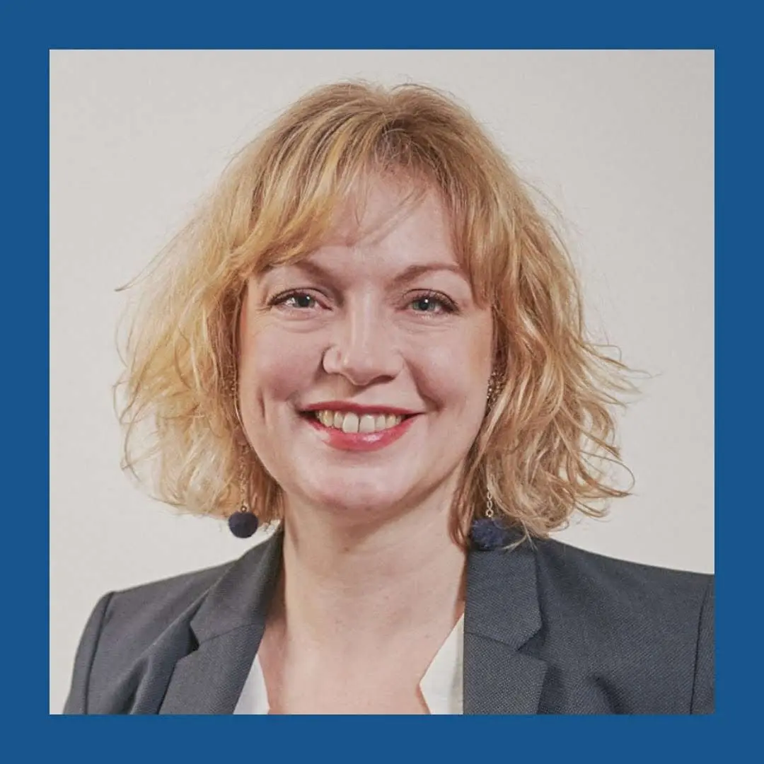 Femme blonde aux yeux bleus regardant et souriant vers la caméra. Bordure bleu foncé.