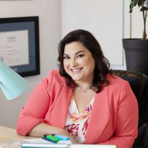 Tania Longpré souriante à son bureau, portant un chandail coloré.